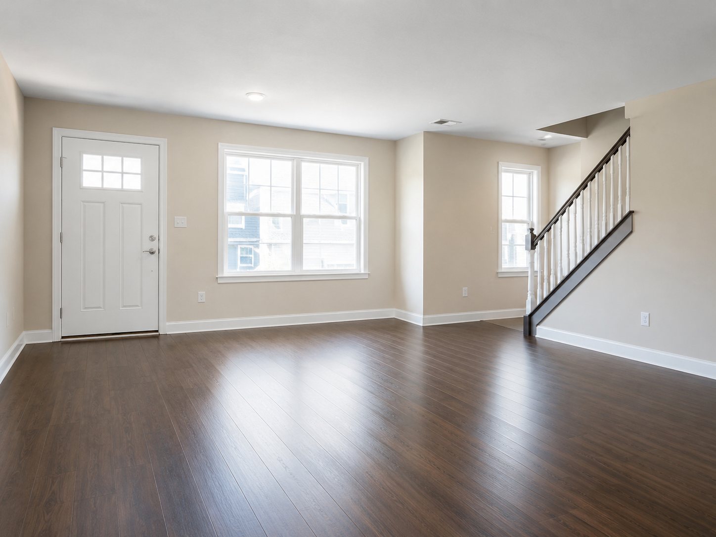 Empty living room with clean hardwood floors, bright windows, and stairs for move-out cleaning